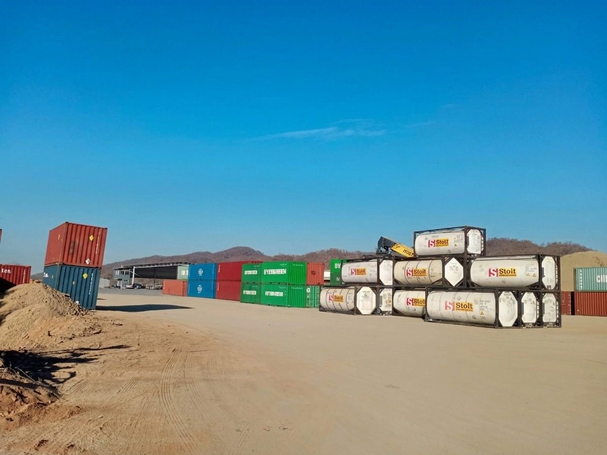 Patio de maniobras con contenedores apilados y tanques ISO bajo un cielo despejado